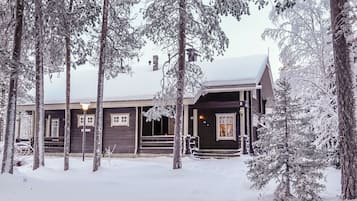 A wooden cabin with a porch, surrounded by snow-covered trees.