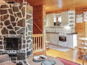 A cozy cabin interior with a stone fireplace, wooden flooring, a kitchen with white cabinets, and a dining area with a table. - Sallanrinne b by Interhome (Salla)