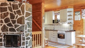 A cozy cabin interior with a stone fireplace, wooden walls, a kitchen with white cabinets, and a dining area with a wooden table. - Sallanrinne b by Interhome (Salla)