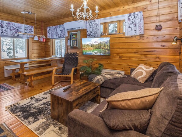 L’intérieur d’un chalet en bois, avec un canapé, un fauteuil, une table et un banc.