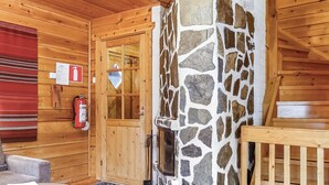 A cozy cabin interior with a stone fireplace, wooden walls, a fire extinguisher, and a red blanket on the wall. - Sallanrinne b by Interhome (Salla)