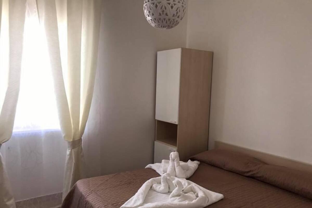 A bedroom with a bed, a bedside table, and a hanging light fixture.