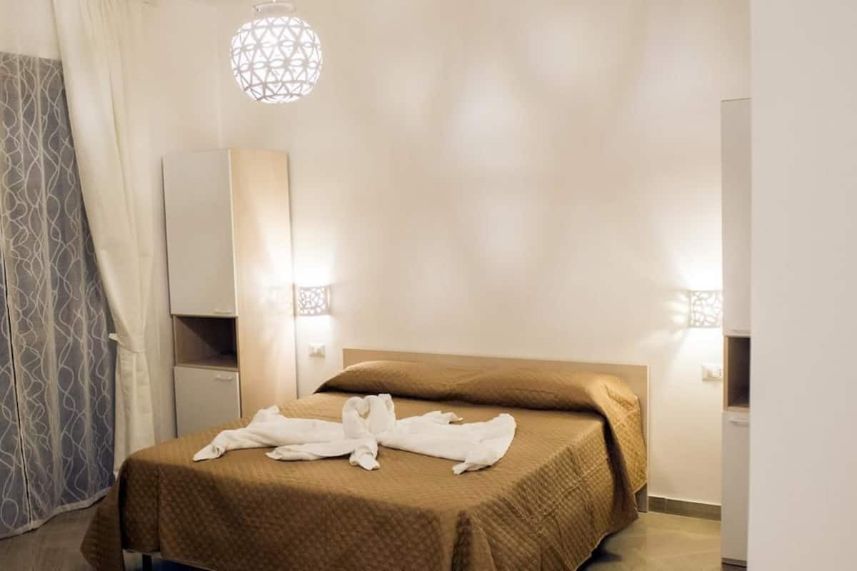 A hotel room with a bed, a wardrobe, a mirror, and two wall-mounted lights.