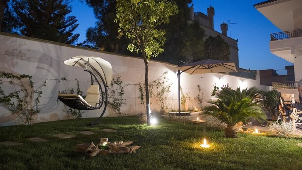 A well-lit outdoor patio area with a dining setup, including a table and chairs, surrounded by a low wall with climbing plants.