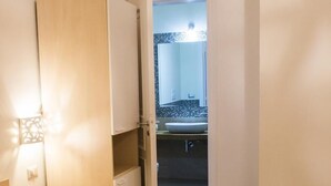 A hotel room with a bed, a bedside table, and a bathroom visible through an open door.