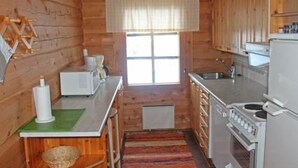 A compact kitchen with wooden walls, a window with blinds, a stove, a sink, and a microwave. - Vacation home Hilla by Interhome (Kittilä)