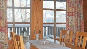 A wooden dining table with chairs, a window with a view of trees, and patterned curtains. - Vacation home Hilla by Interhome (Kittilä)