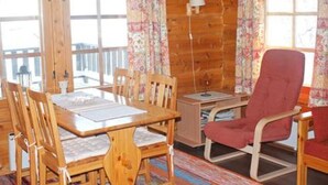 A wooden cabin interior with a dining table, chairs, a red cushioned chair, and a window with curtains. - Vacation home Hilla by Interhome (Kittilä)