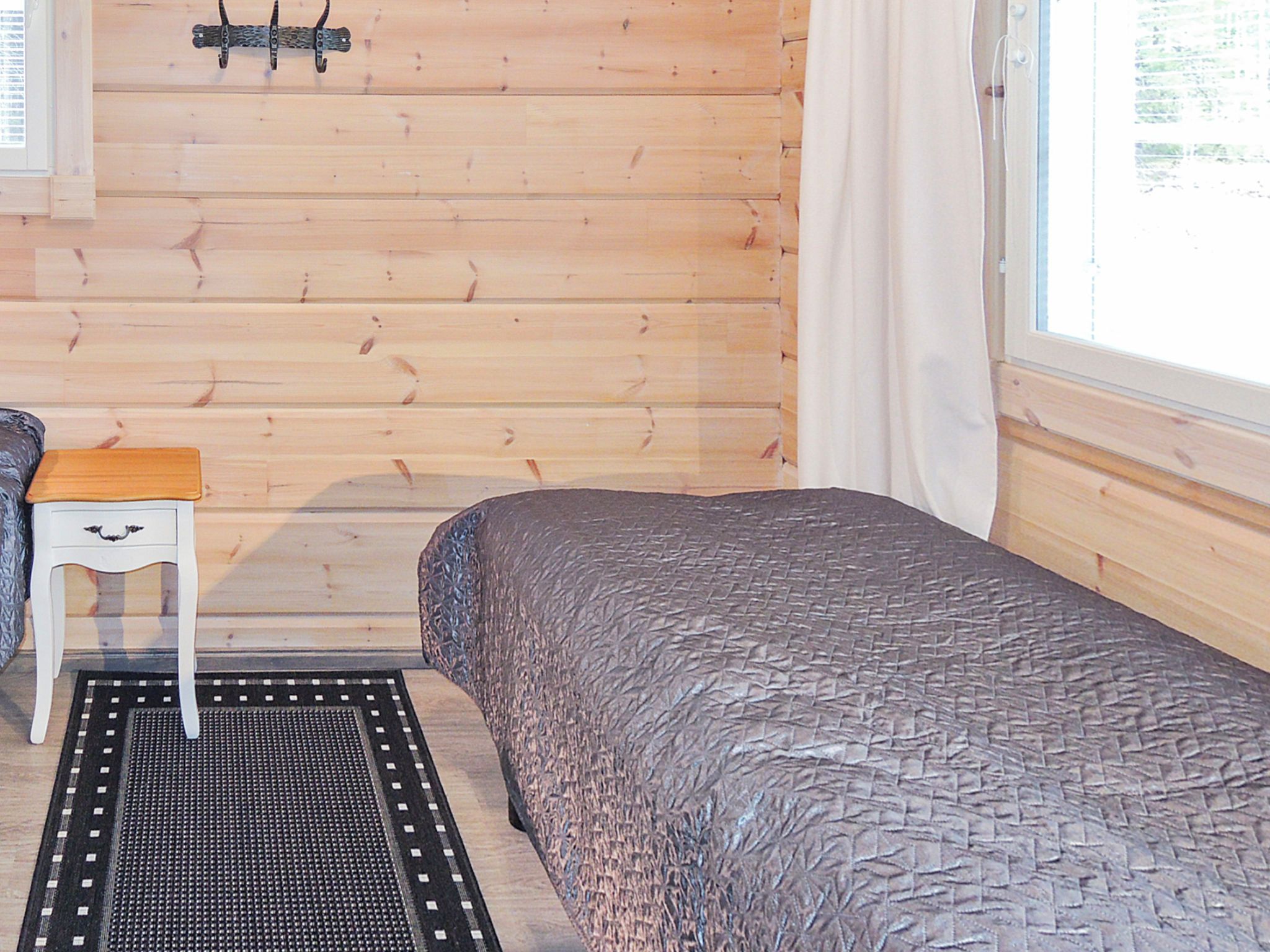Ein Zimmer in einer Holzhütte mit einem Bett, einem kleinen Tisch und einem Fenster.