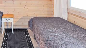 Ein Zimmer in einer Holzhütte mit einem Bett, einem kleinen Tisch und einem Fenster.
