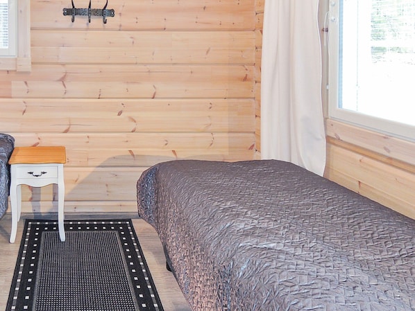 Una habitación de cabaña de madera con una cama, una mesita y un ventanal.