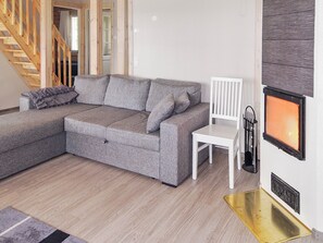 A modern living room with a grey sectional sofa, a white chair, a fireplace, and a staircase. - Nesterin helmi by Interhome (Eno)