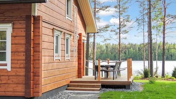 A wooden cabin with a deck overlooking a lake, surrounded by trees. - Nesterin helmi by Interhome (Eno)