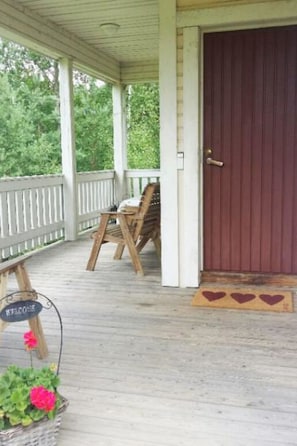 A covered porch with a wooden bench and a chair, a red door, and a welcome sign. - Hurran ranta by Interhome (Somero)