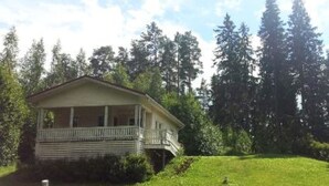 A single-story house with a porch, surrounded by a grassy yard and tall trees.