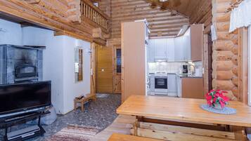 Interior de una cabaña de troncos con televisión, mesa de comedor de madera y zona de cocina.