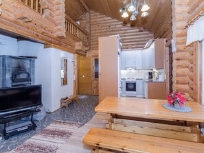 L’intérieur d’une cabane en rondins, avec un téléviseur, une table à manger en bois et un coin cuisine.