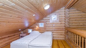 Un dormitorio tipo cabaña de madera con cama en el altillo, paredes de madera y techo inclinado.