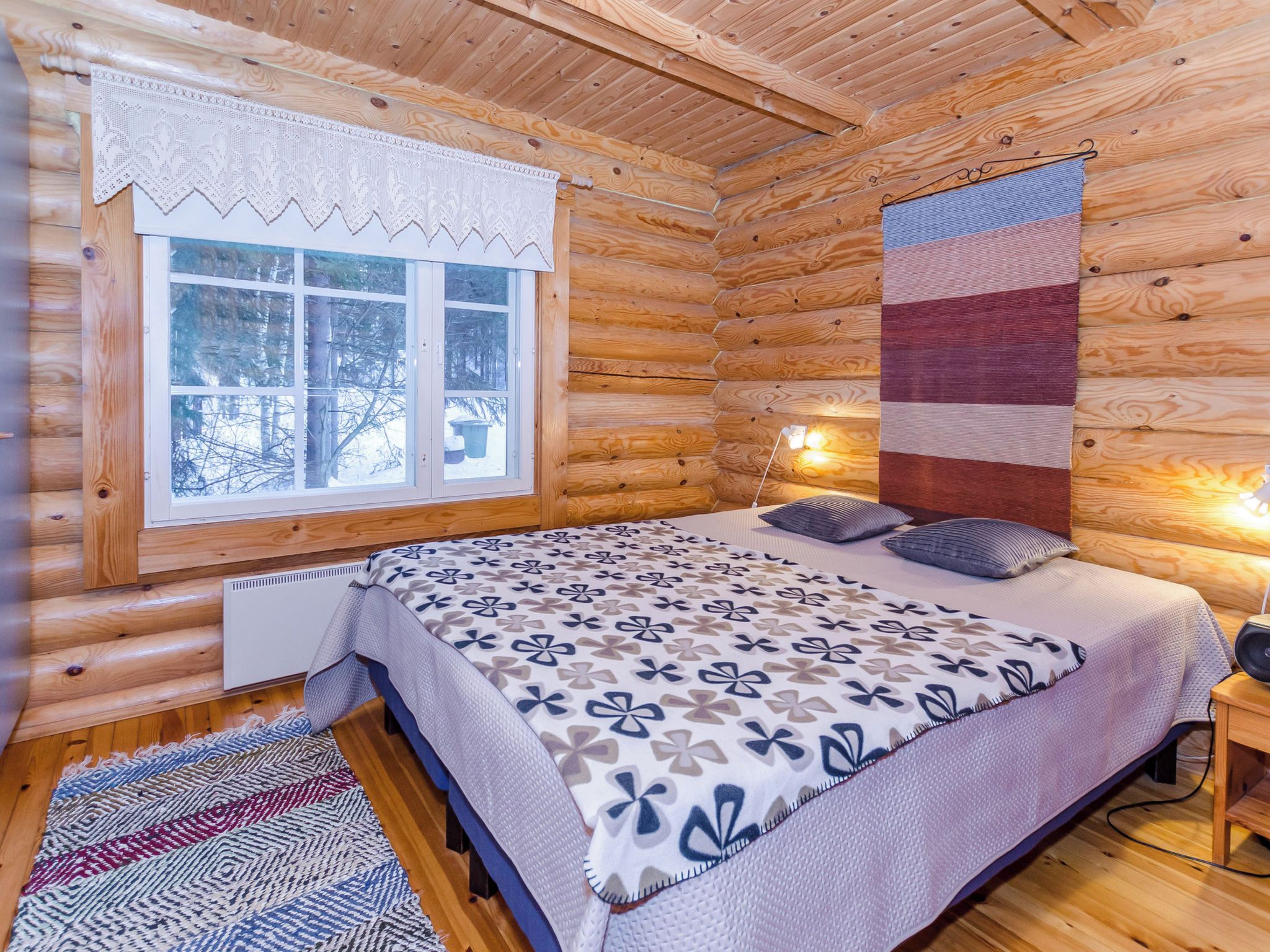 A log cabin bedroom with a bed, a window, a quilt, and a wall hanging.