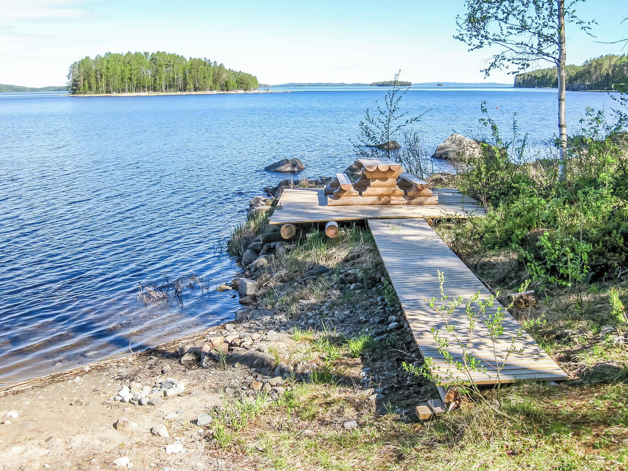 En träbrygga som sträcker sig ut i en stilla sjö, med en skogbeklädd ö i fjärran.