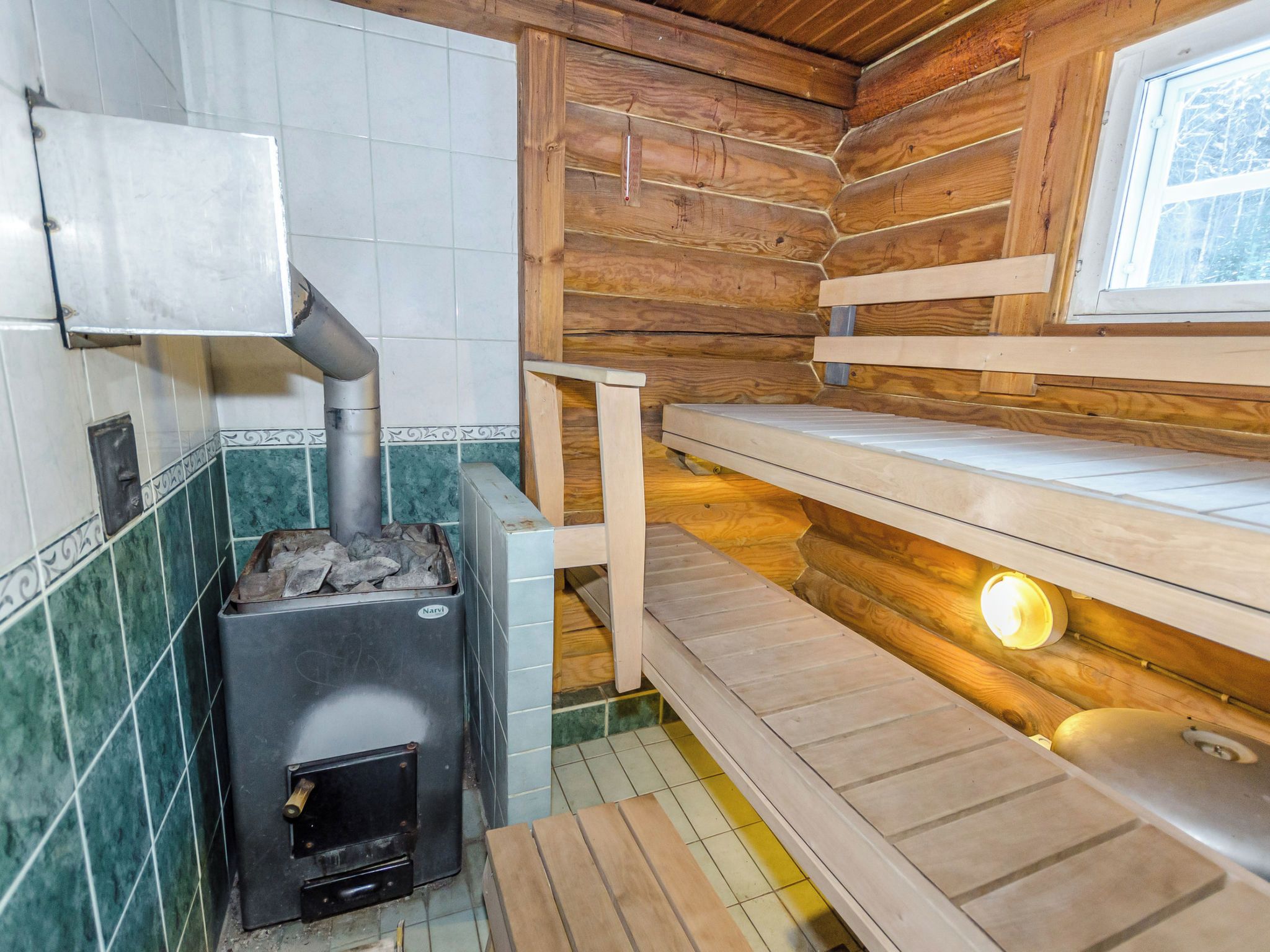 Ein Holzblock-Interieur mit Holzofen, Kachelwänden und einem Fenster.