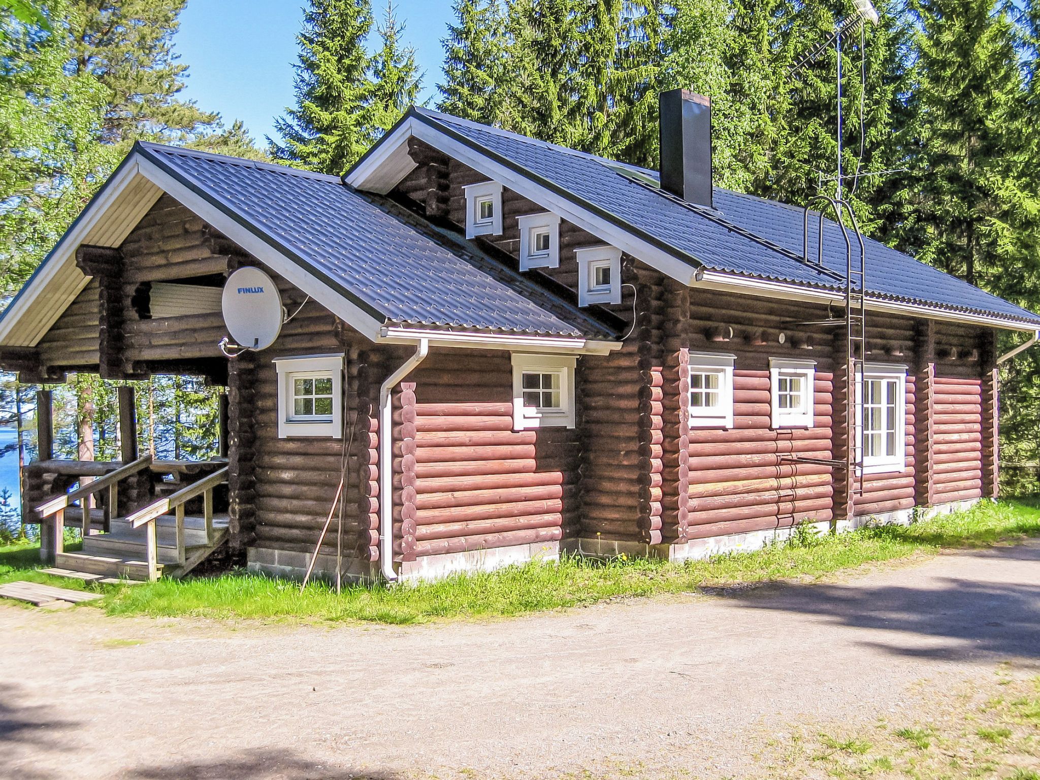 A log cabin with a porch, a chimney, and a satellite dish.