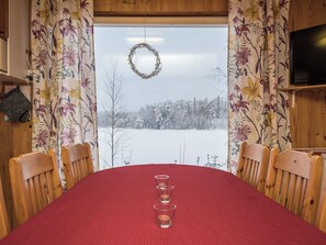 Ruokapöytä, jonka päällä on punainen pöytäliina, ja pöydän ympärillä on puisia tuoleja sekä kynttilöitä.