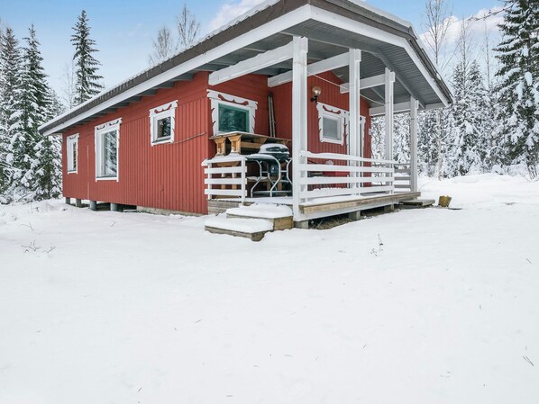 A red cabin with a white porch, surrounded by snow-covered trees.