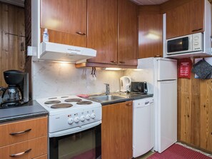 Una cocina compacta con gabinetes de madera, estufa blanca, microondas y lavavajillas.