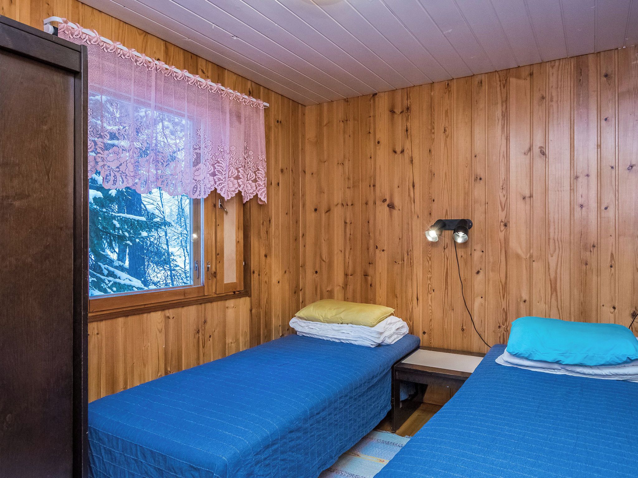 A cabin with two single beds, a window with a lace curtain, and a wall-mounted light fixture.