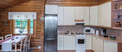 A compact kitchen with wooden walls, a refrigerator, stove, microwave, and a sink.