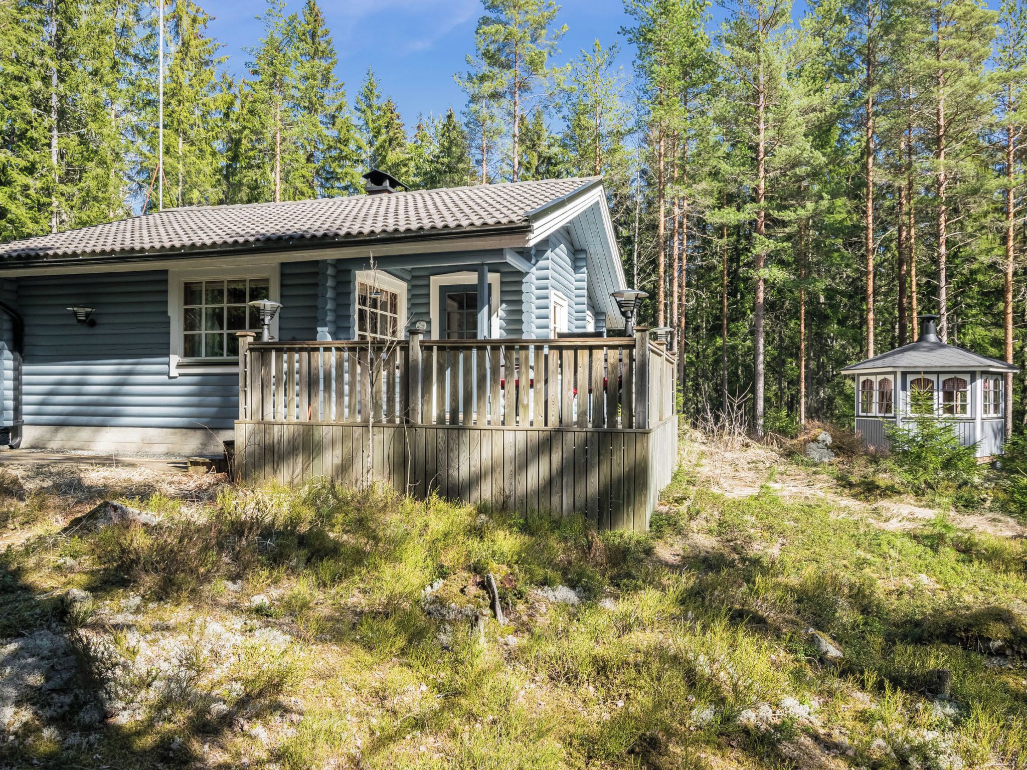 A cabin with a wooden deck, a small attached structure, surrounded by a forest.