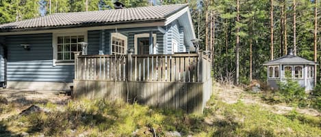 A cabin with a wooden deck, a small attached structure, surrounded by a forest.