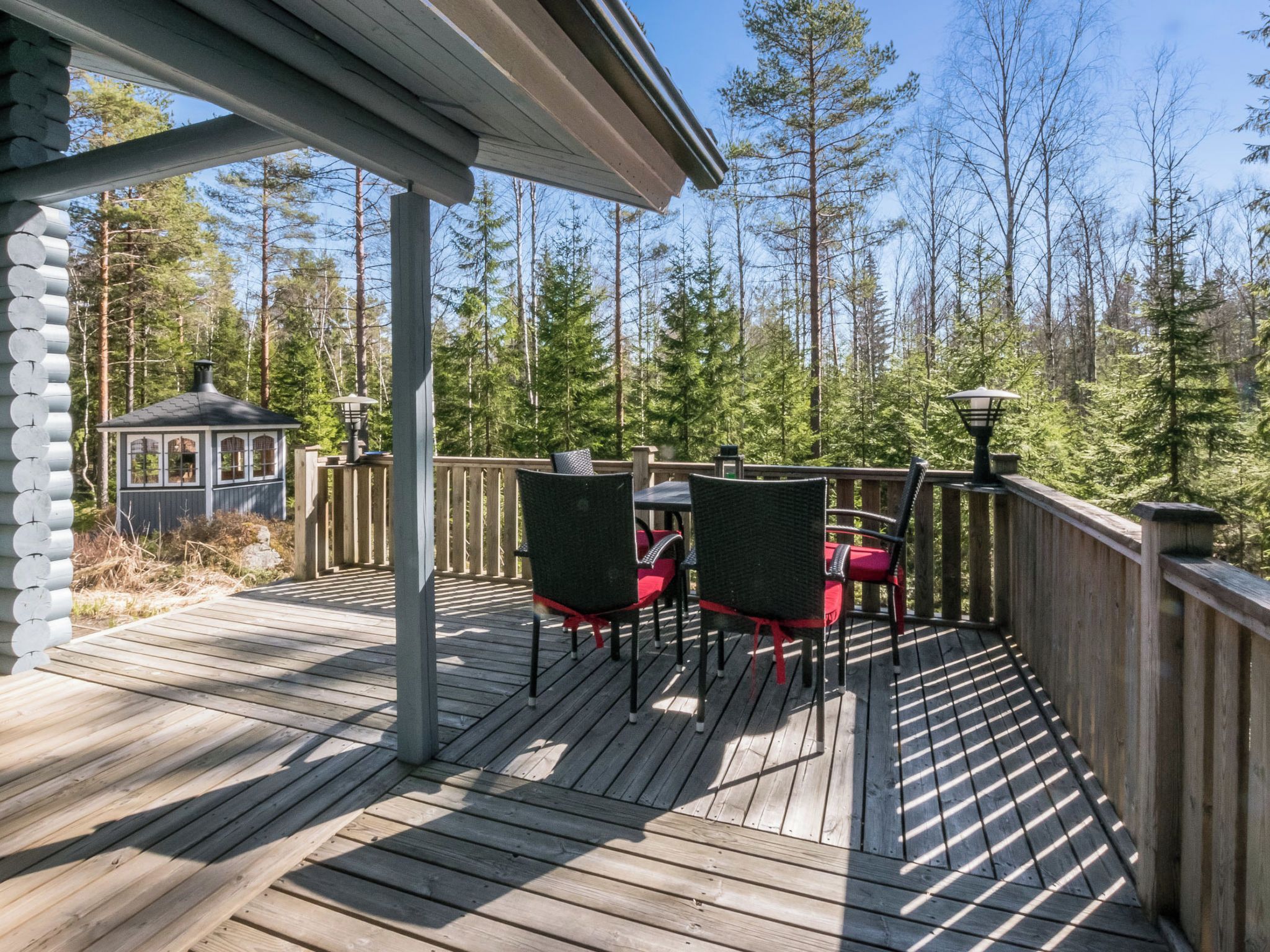 A wooden deck with outdoor furniture, a gazebo, and a forested backdrop.