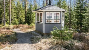 Una cabaña pequeña con chimenea, ventanas y puerta, rodeada de un bosque.