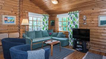 A log cabin interior with a sofa, chairs, a TV, and a fireplace.