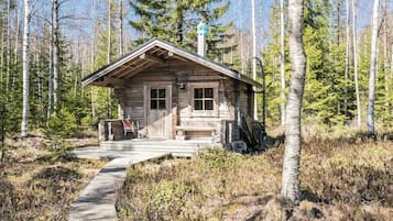 Une cabane rustique dotée d’un porche en bois, d’un banc et d’un espace abrité avec une cheminée.