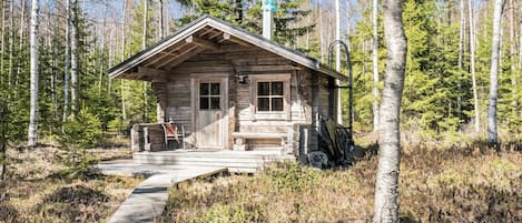 A rustic cabin with a wooden porch, a bench, and a covered area with a chimney.
