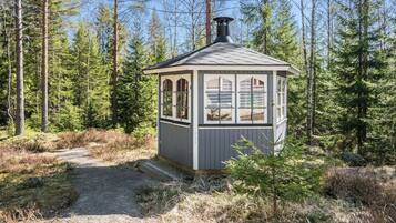 A small cabin with a single window and a chimney, surrounded by a forest.