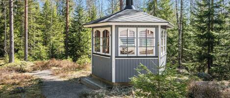 A small cabin with a single window and a chimney, surrounded by a forest.