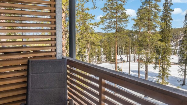 Un balcon doté d’une balustrade en bois, d’une chaise et offrant une vue sur un paysage enneigé parsemé d’arbres.
