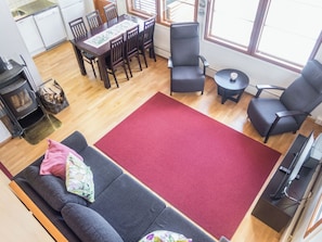 Ein Wohnzimmer mit einer Couch, einem roten Teppich, einem Kamin, einem Esstisch mit Stühlen und einem Fernseher.