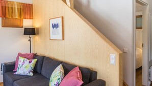 Un salon avec un escalier, un canapé agrémenté de coussins colorés, un tableau encadré au mur et une lampe.