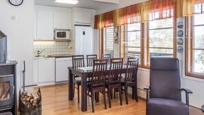 Une cuisine moderne avec des meubles blancs, un four à micro-ondes et un lave-vaisselle. On y trouve un coin repas avec une table et des chaises en bois, ainsi qu’une grande fenêtre avec des rideaux.