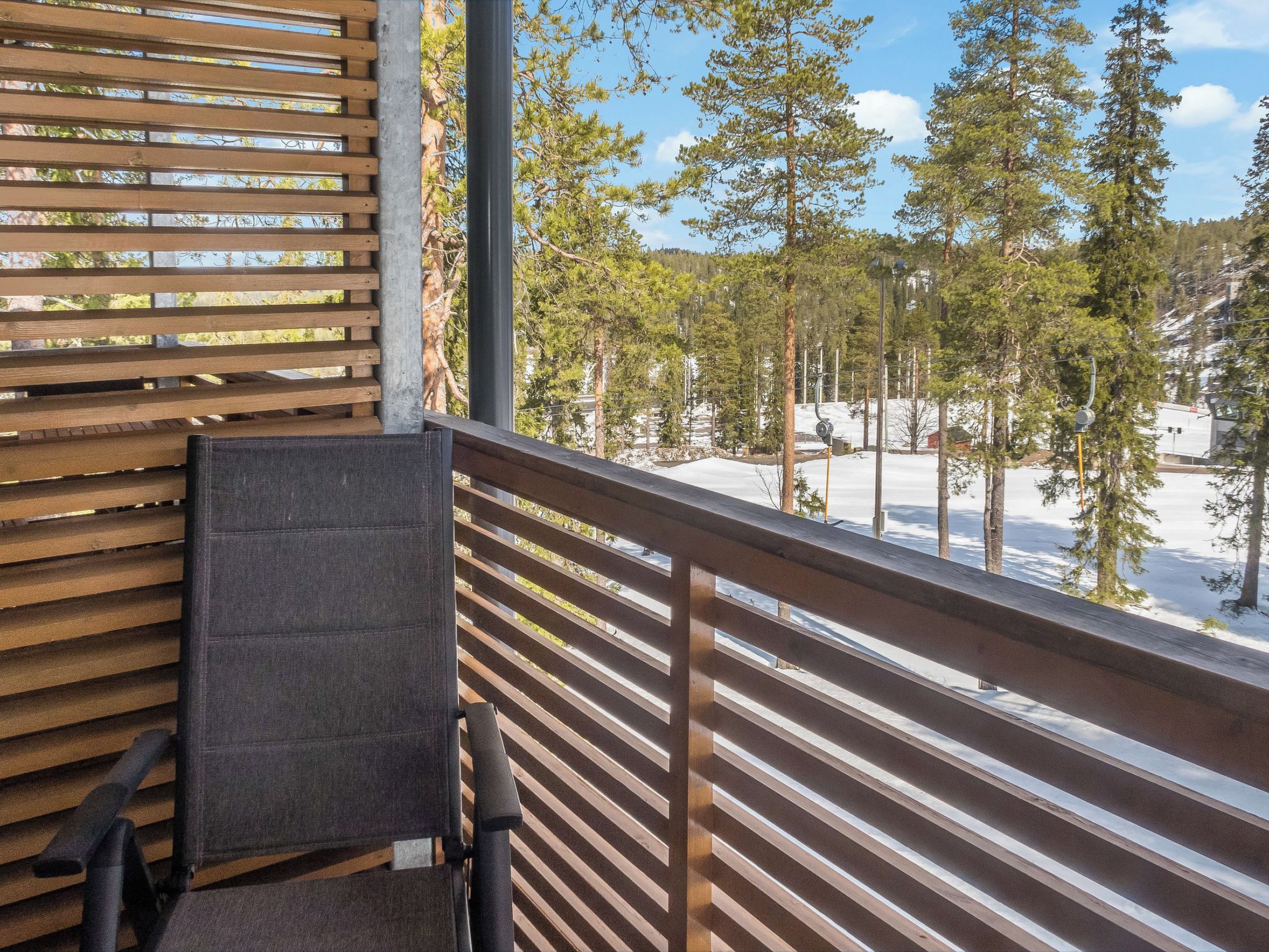 A balcony with a wooden railing, a chair, and a view of a snowy landscape with trees.