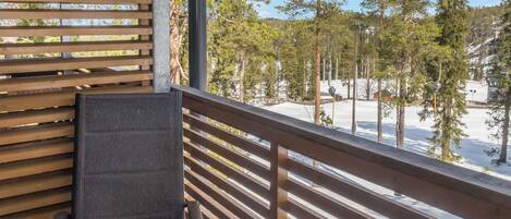 Ein Balkon mit Holzwertung, einem Stuhl und Blick auf eine verschneite Landschaft mit Bäumen.