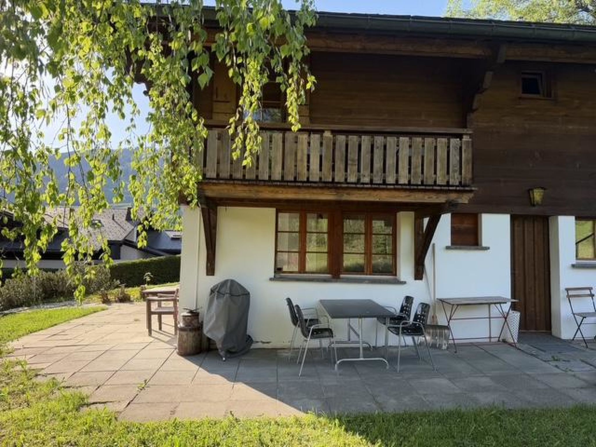 Une maison en bois avec un balcon, une terrasse avec une table et des chaises, et un barbecue.