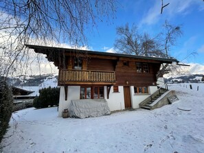 A wooden chalet with a balcony, a covered porch, and a staircase leading to the entrance.
