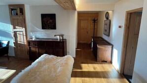 A room with wooden floors, a white fluffy rug, a wooden cabinet, a painting, and a coat rack.