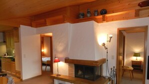 Ein gemütliches Wohnzimmer mit Kamin, Holzbalken und einer Küche im Hintergrund.